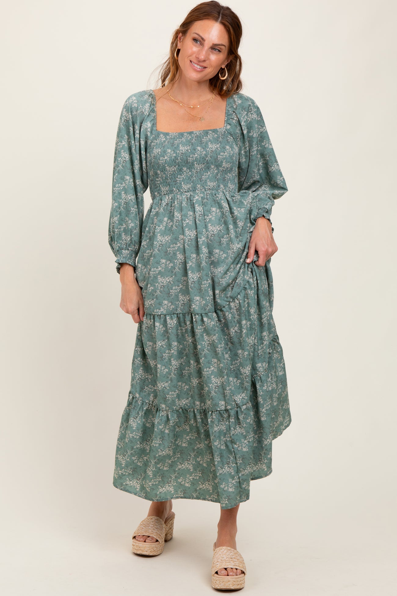 woman wearing a teal floral maxi dress with square neckline and puff sleeves, standing with a smile