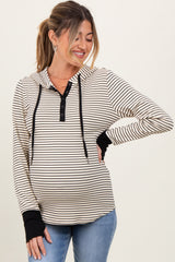 woman wearing a cream and black striped maternity hoodie with a button-up neckline and black cuffs, showing her baby bump