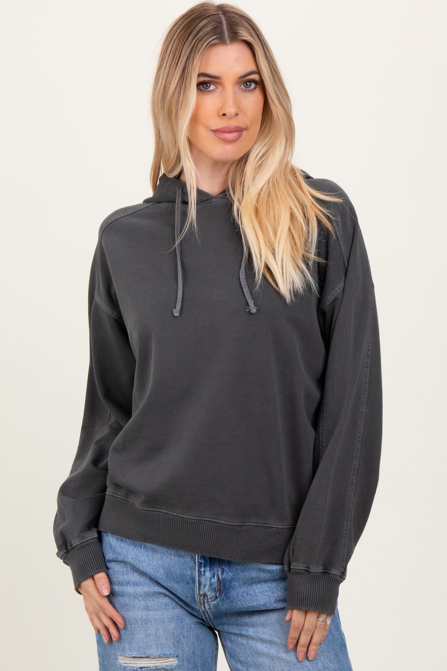 woman wearing a dark gray oversized hoodie with a drawstring and relaxed fit, paired with light blue jeans