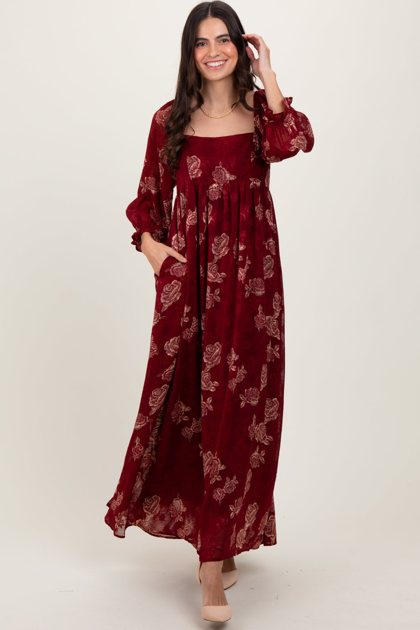 woman wearing a burgundy floral maxi dress with long sleeves and pockets, smiling at the camera
