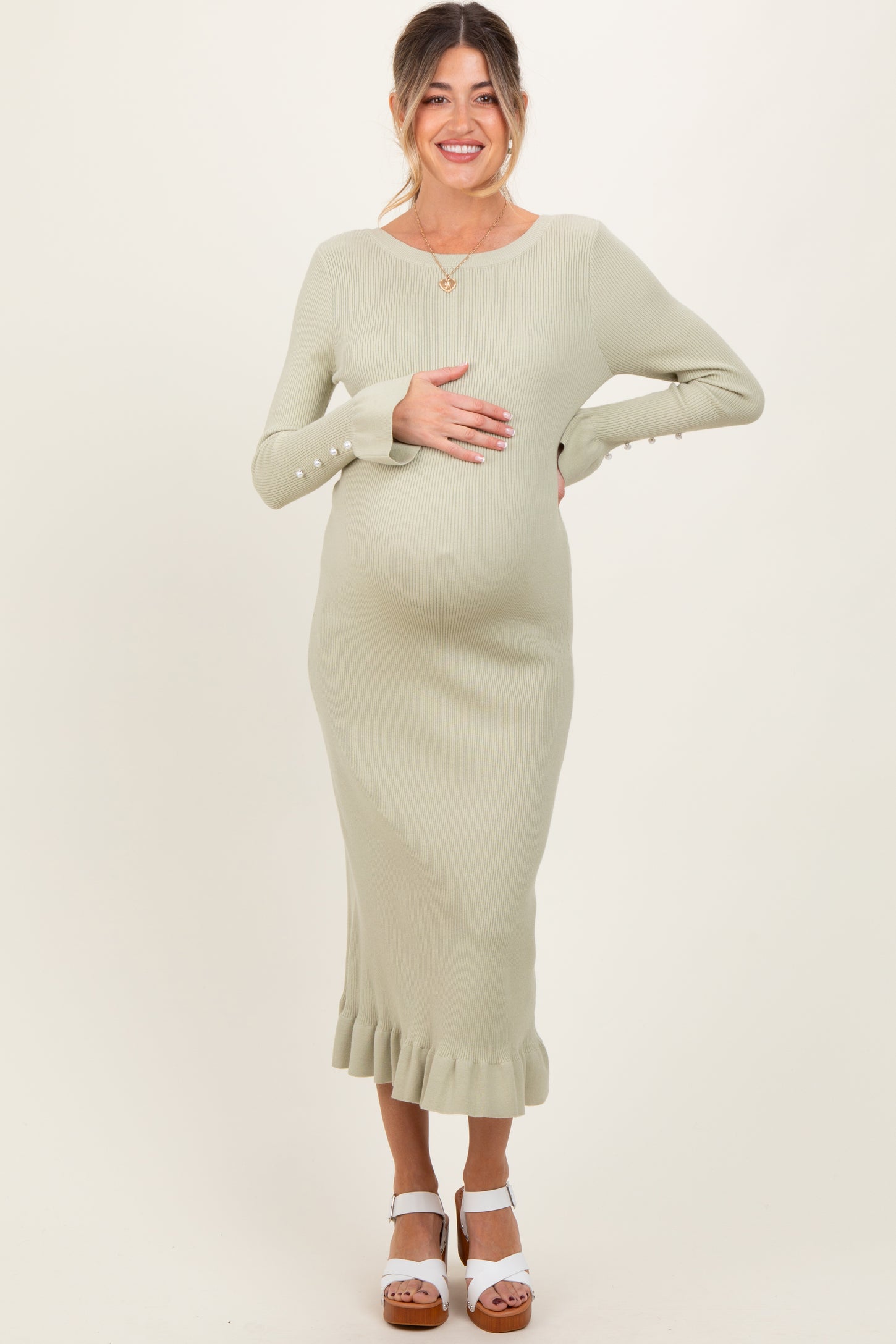 woman wearing a light green ribbed maternity dress with a ruffled hem and buttons on the sleeves, showing her baby bump