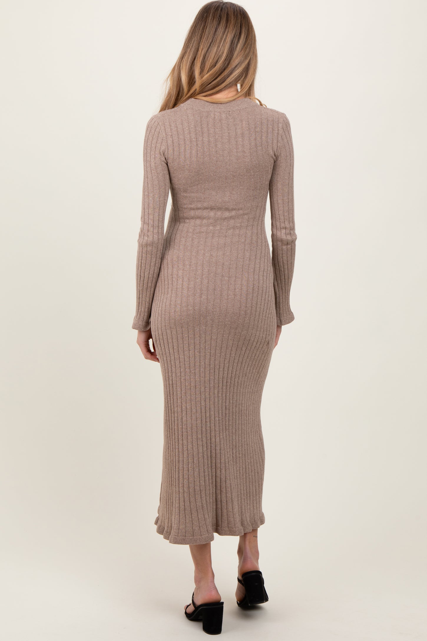 woman wearing a beige ribbed maternity dress with long sleeves, showing a fitted silhouette and mid-calf length