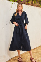 woman wearing a navy blue long sleeve button-up dress with a tie waist detail standing against a textured wall