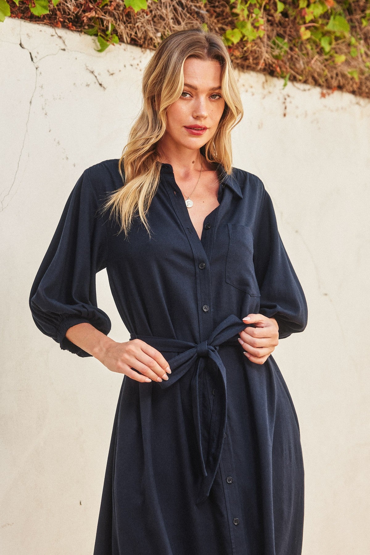woman wearing a navy blue button-up shirt dress with a tie waist and balloon sleeves