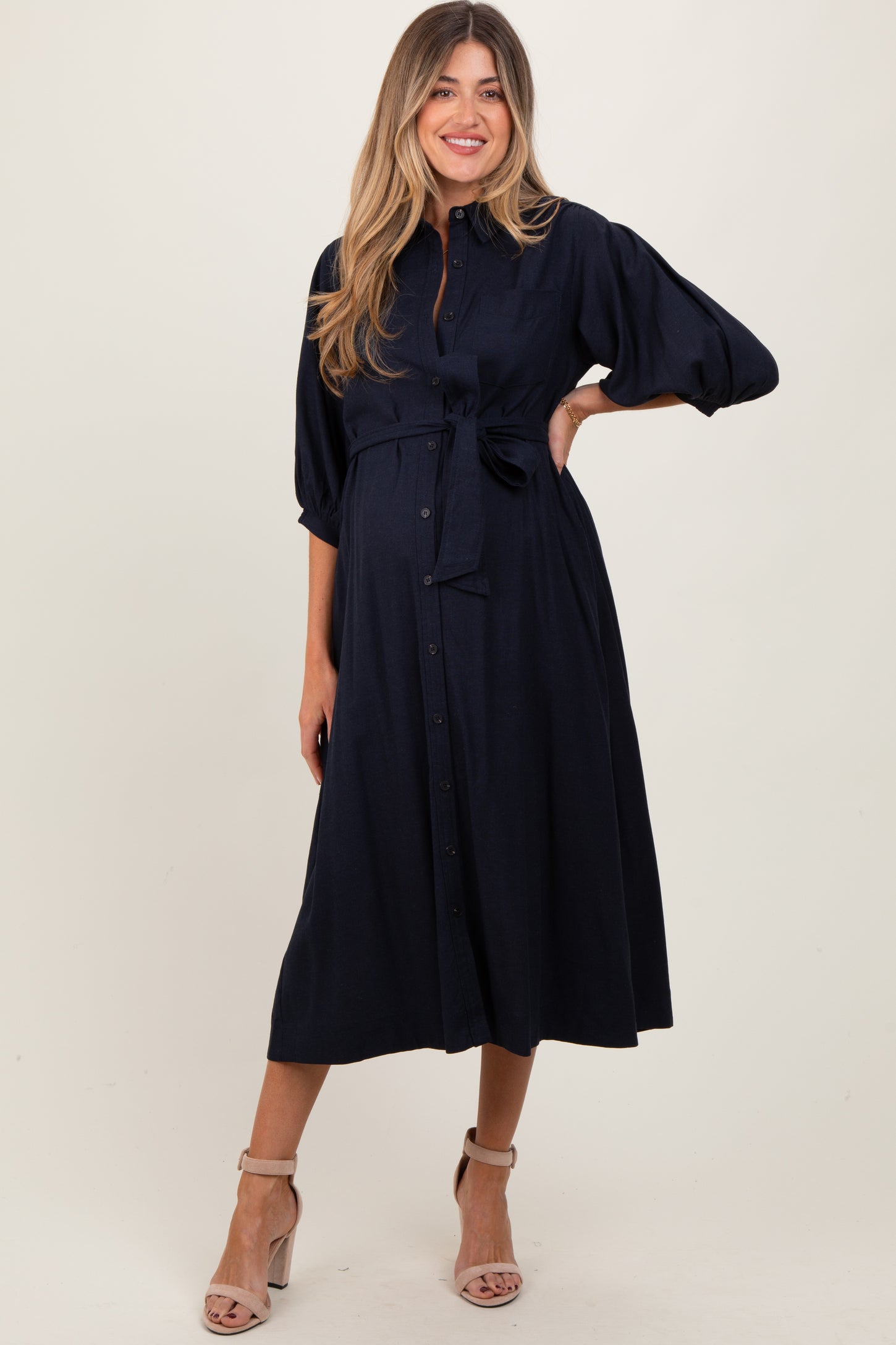 woman wearing a navy blue maternity dress with a tied waist and three-quarter sleeves, showing her baby bump
