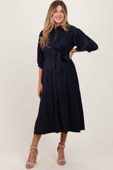 woman wearing a navy blue maternity dress with a tied waist and three-quarter sleeves, showing her baby bump