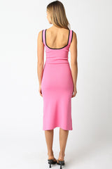 woman wearing a fitted pink midi dress with black strap detailing, showing a bare back