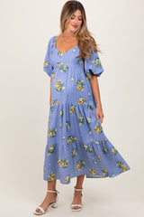 woman wearing a floral print maternity dress in light blue with short puff sleeves and a tiered skirt, showing her baby bump