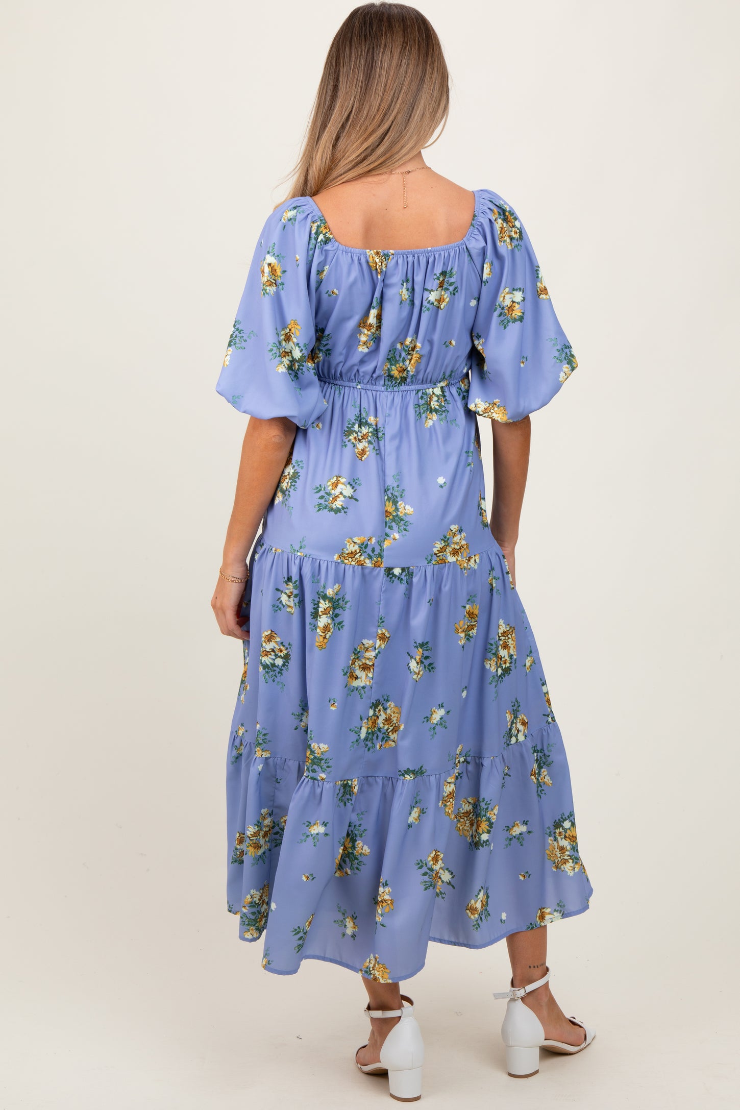 woman wearing a blue floral maternity dress with a tiered skirt and puff sleeves, showing her baby bump from the back
