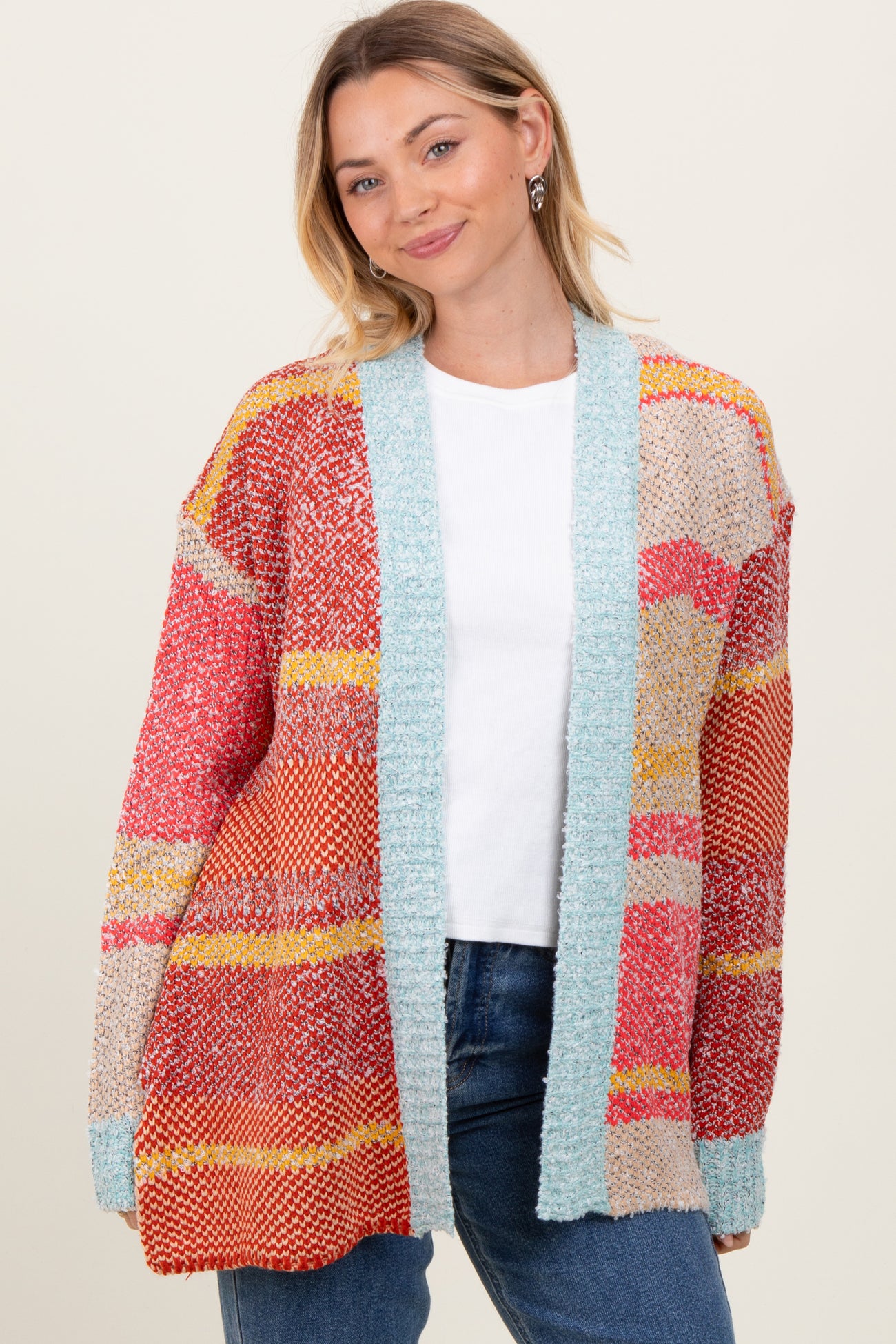 woman wearing a colorful oversized cardigan with red, orange, and blue details over a white top and jeans