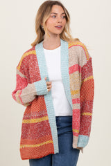 woman wearing a multicolored oversized cardigan with patterns in red, orange, and turquoise over a white top and jeans