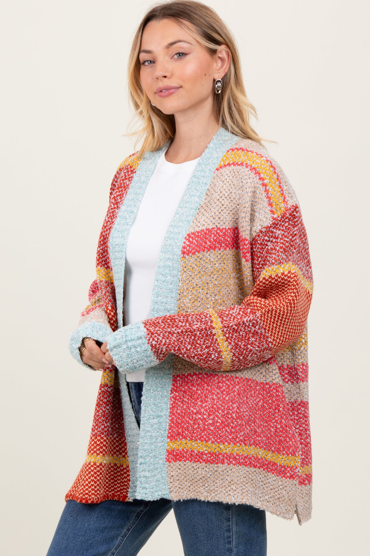 woman wearing a multicolored oversized cardigan featuring stripes and a blue trim, styled with a white top and jeans