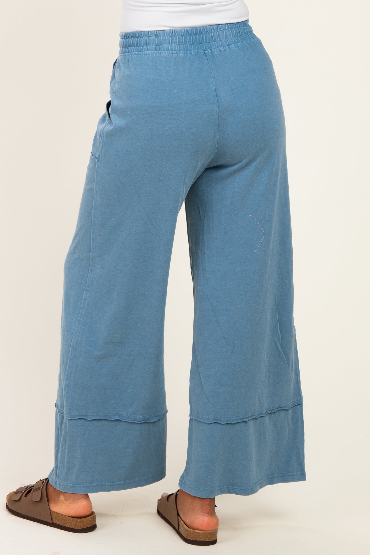 woman wearing blue wide leg pants with an elastic waistband and side pockets, shown from the back