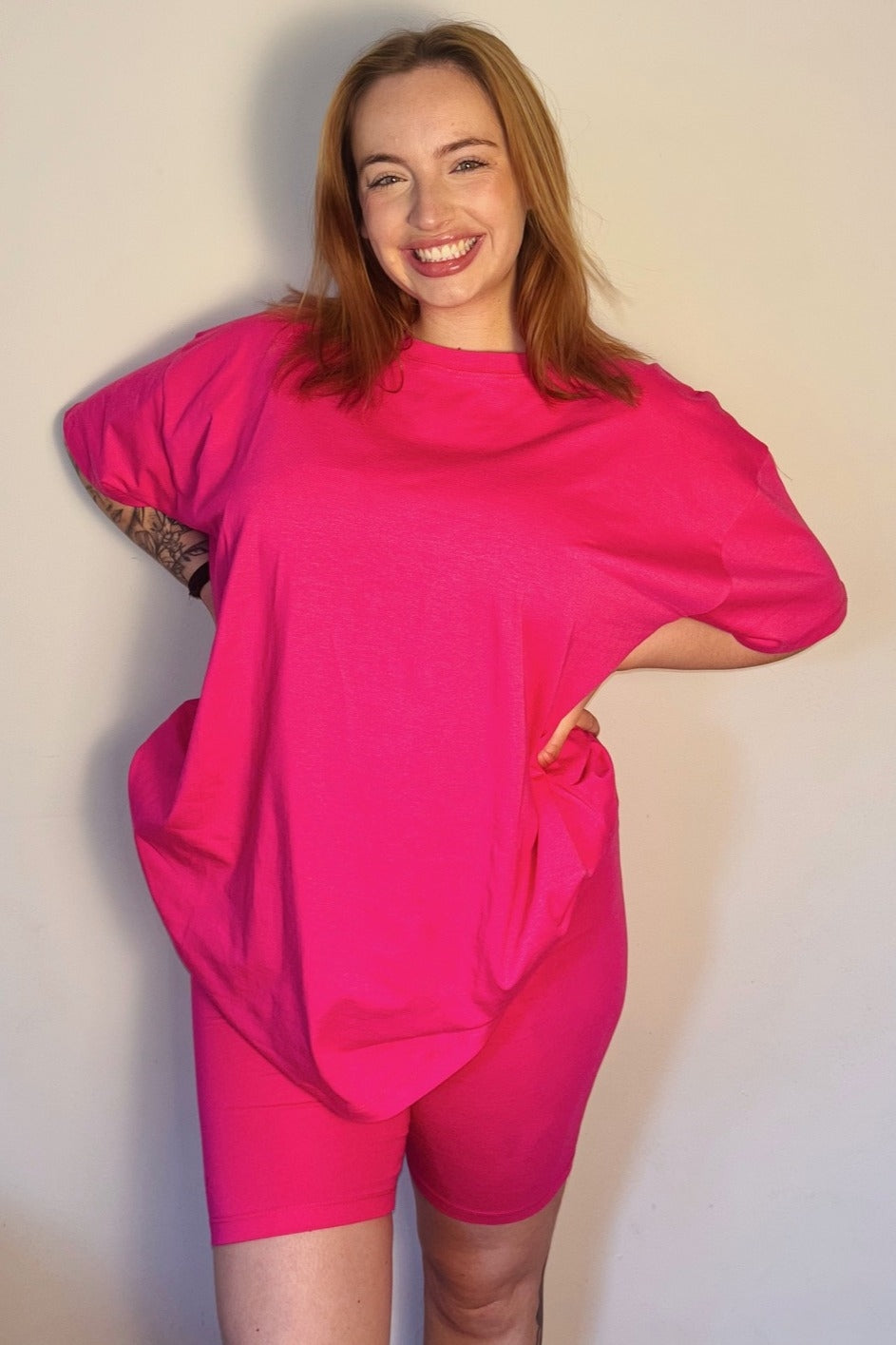 woman wearing a bright pink maternity t-shirt and matching shorts, smiling and posing with her hands on her hips