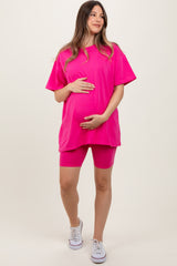 woman wearing a hot pink maternity oversized t-shirt and matching bike shorts, gently holding her baby bump
