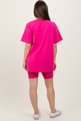 woman wearing a bright pink oversized t-shirt and matching bike shorts, showcasing a casual maternity outfit