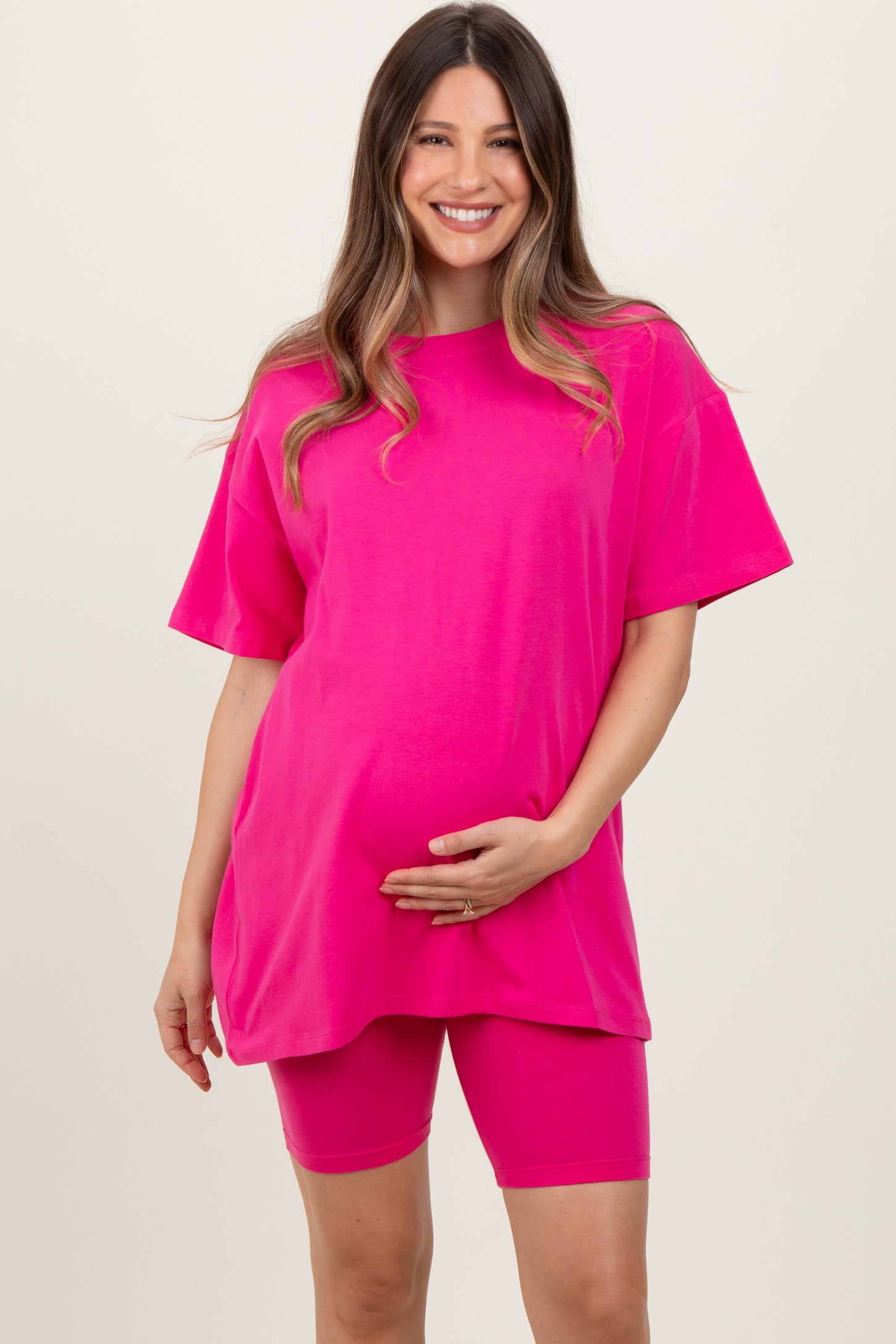 woman wearing a bright pink oversized maternity t-shirt and matching bike shorts, holding her baby bump