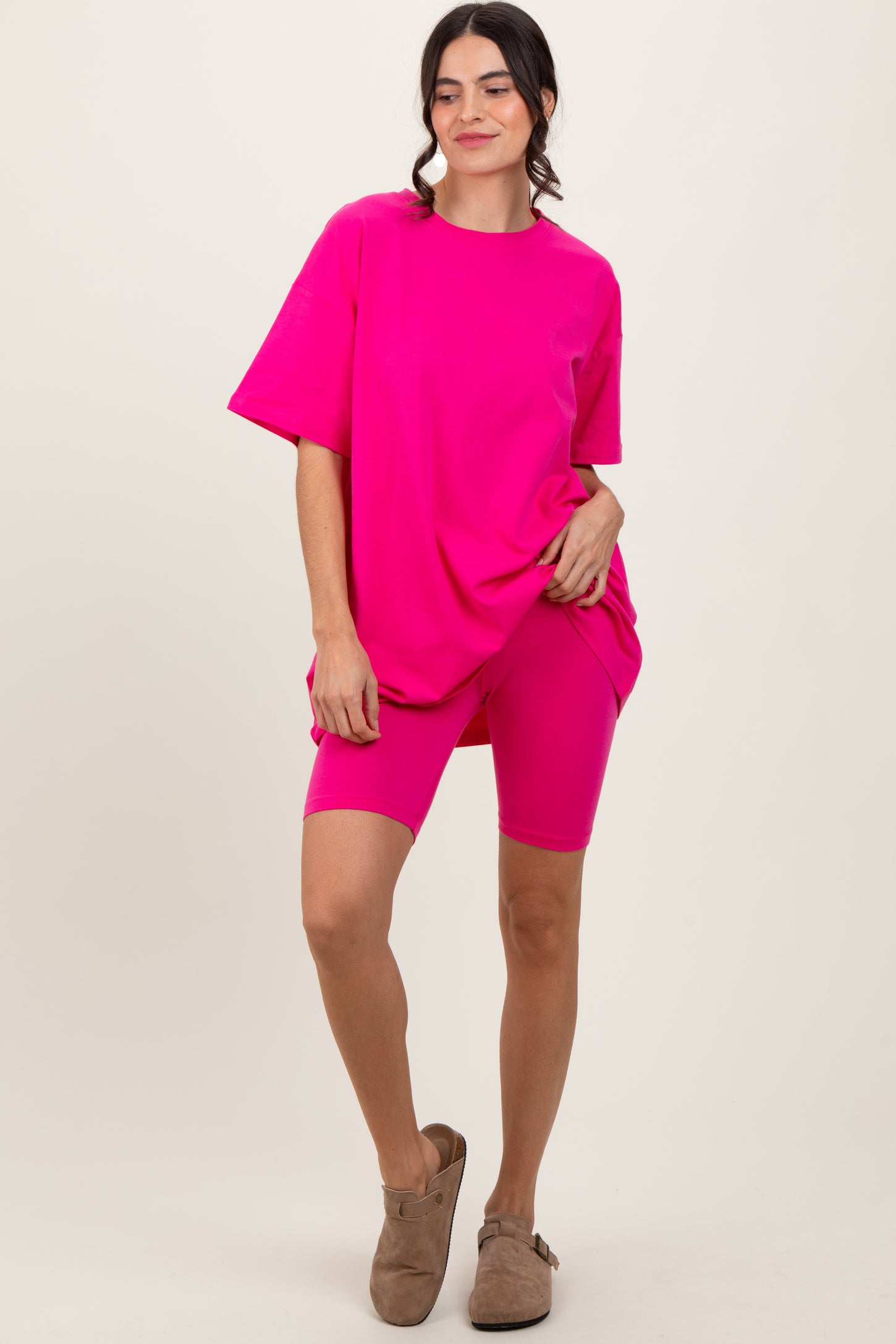 woman wearing a bright pink oversized t-shirt and matching biker shorts, standing with one hand on hip