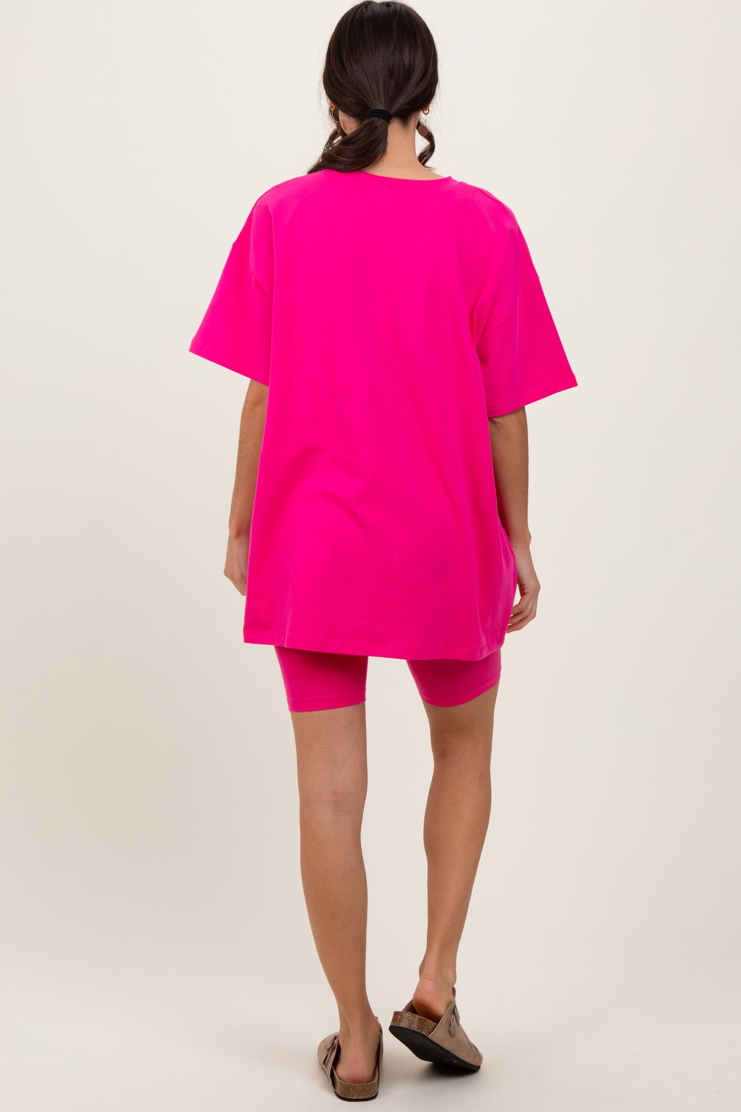 woman wearing a bright pink oversized t-shirt and matching biker shorts, viewed from the back