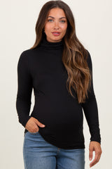 woman wearing a black long sleeve maternity turtleneck top and blue jeans, with a visible baby bump