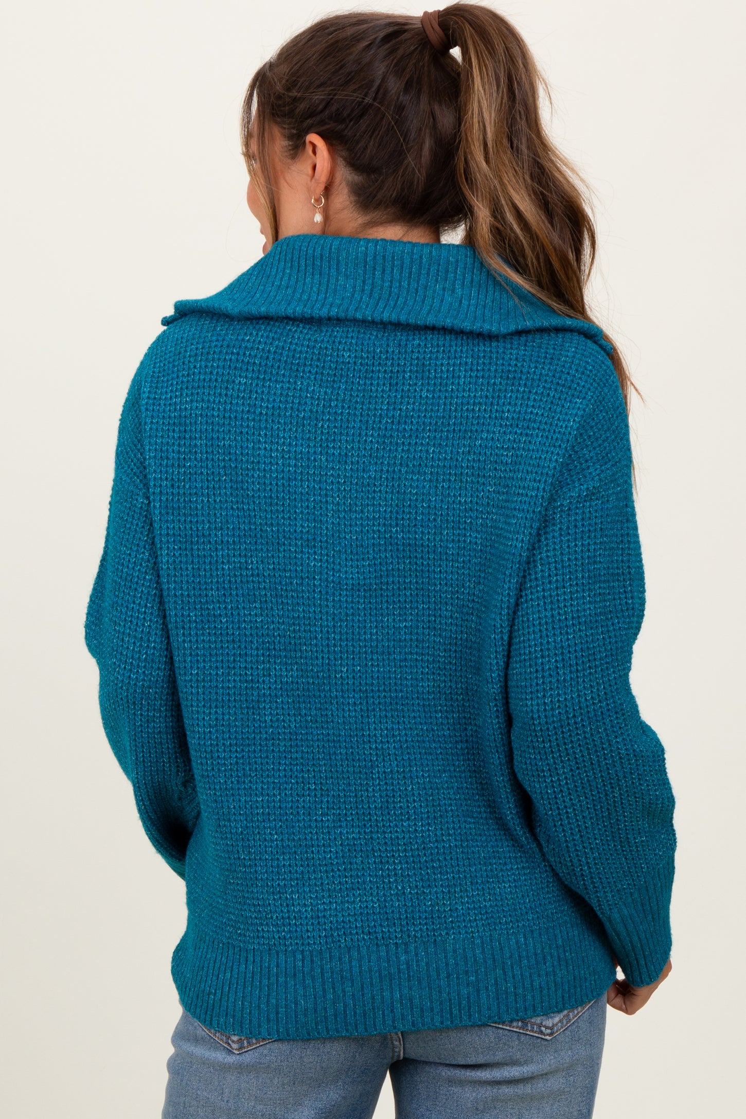 woman wearing a teal maternity sweater with a large collar and relaxed fit, showing the back view