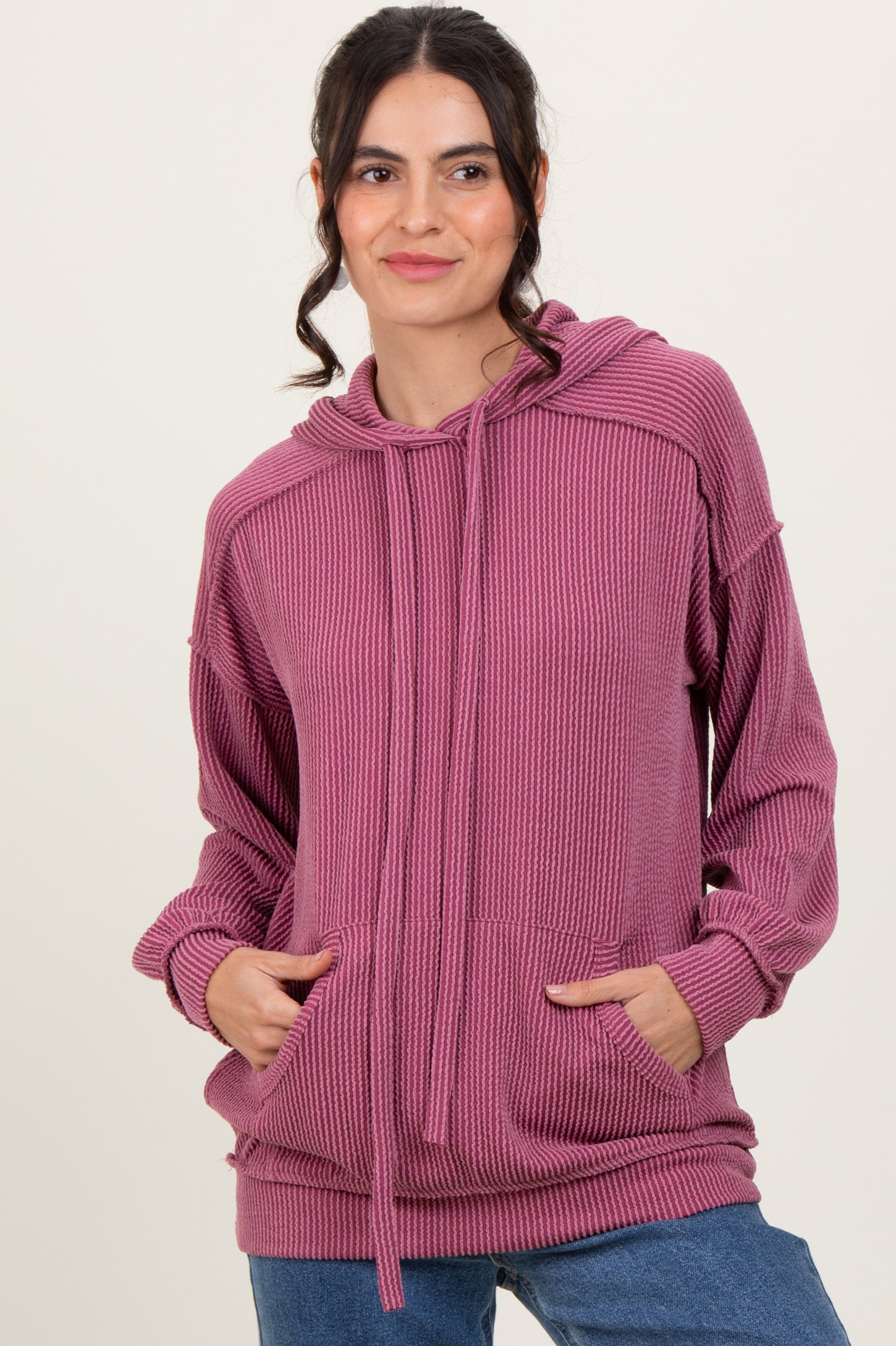woman wearing a light pink ribbed hoodie with a front pocket and drawstring, styled with blue jeans