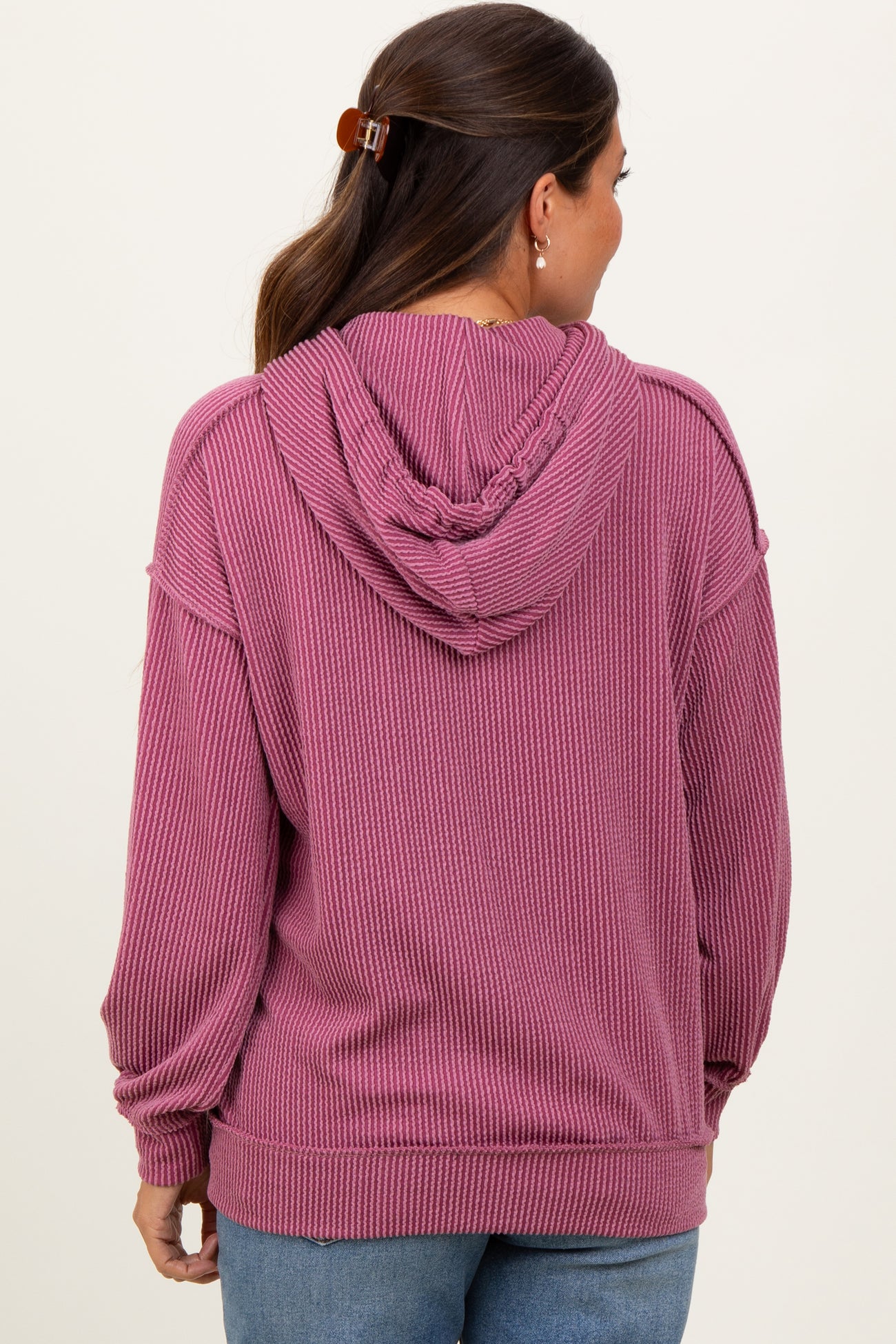 woman wearing a pink ribbed maternity hoodie with a drawstring hood and a relaxed fit, showing a baby bump from the back