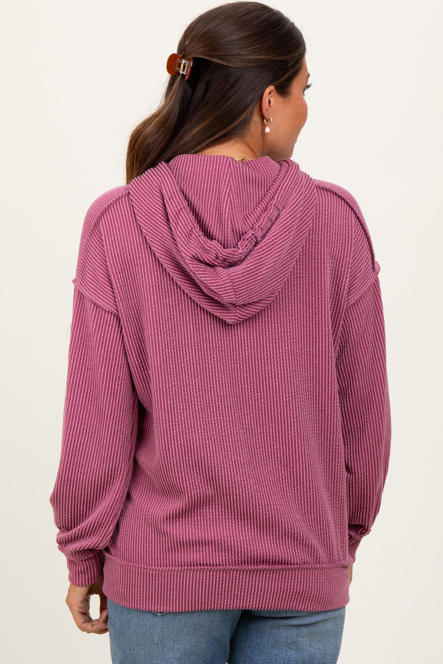 woman wearing a pink ribbed maternity hoodie with a drawstring hood and a relaxed fit, showing a baby bump from the back