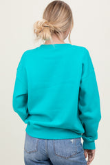 woman wearing a vibrant teal oversized sweatshirt with a relaxed fit, viewed from the back