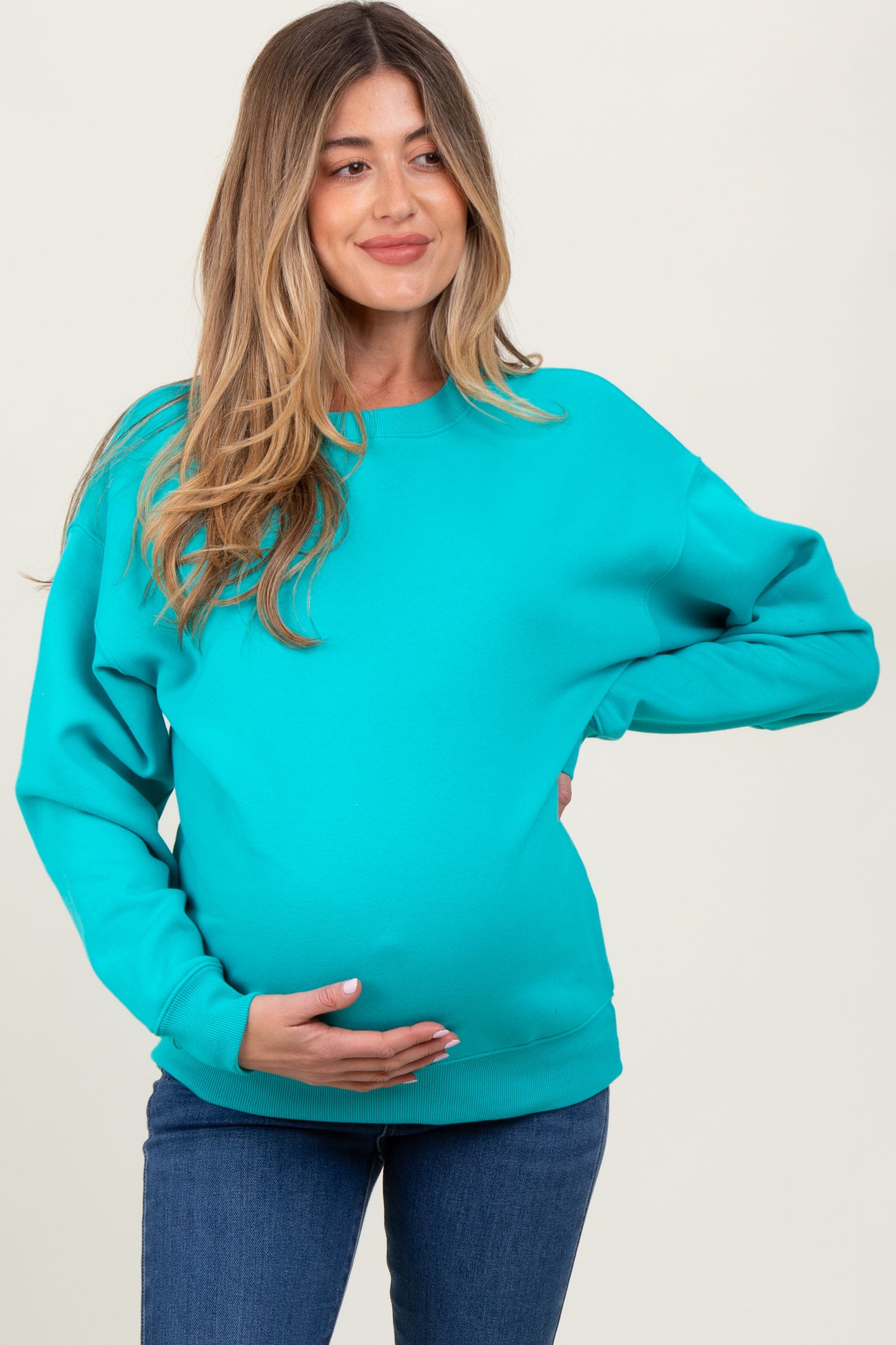 woman wearing a bright turquoise maternity sweatshirt and holding her baby bump