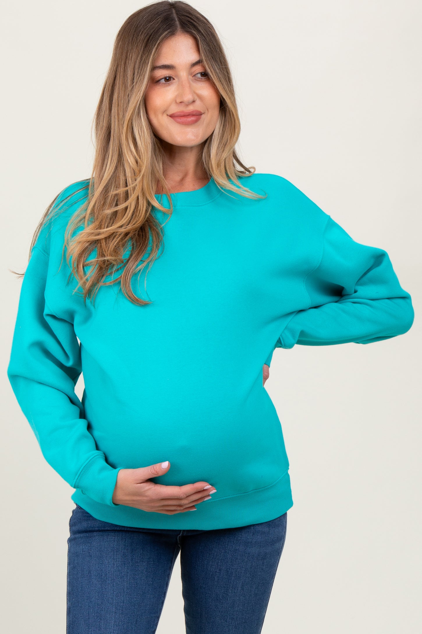 woman wearing a bright turquoise maternity sweatshirt and holding her baby bump