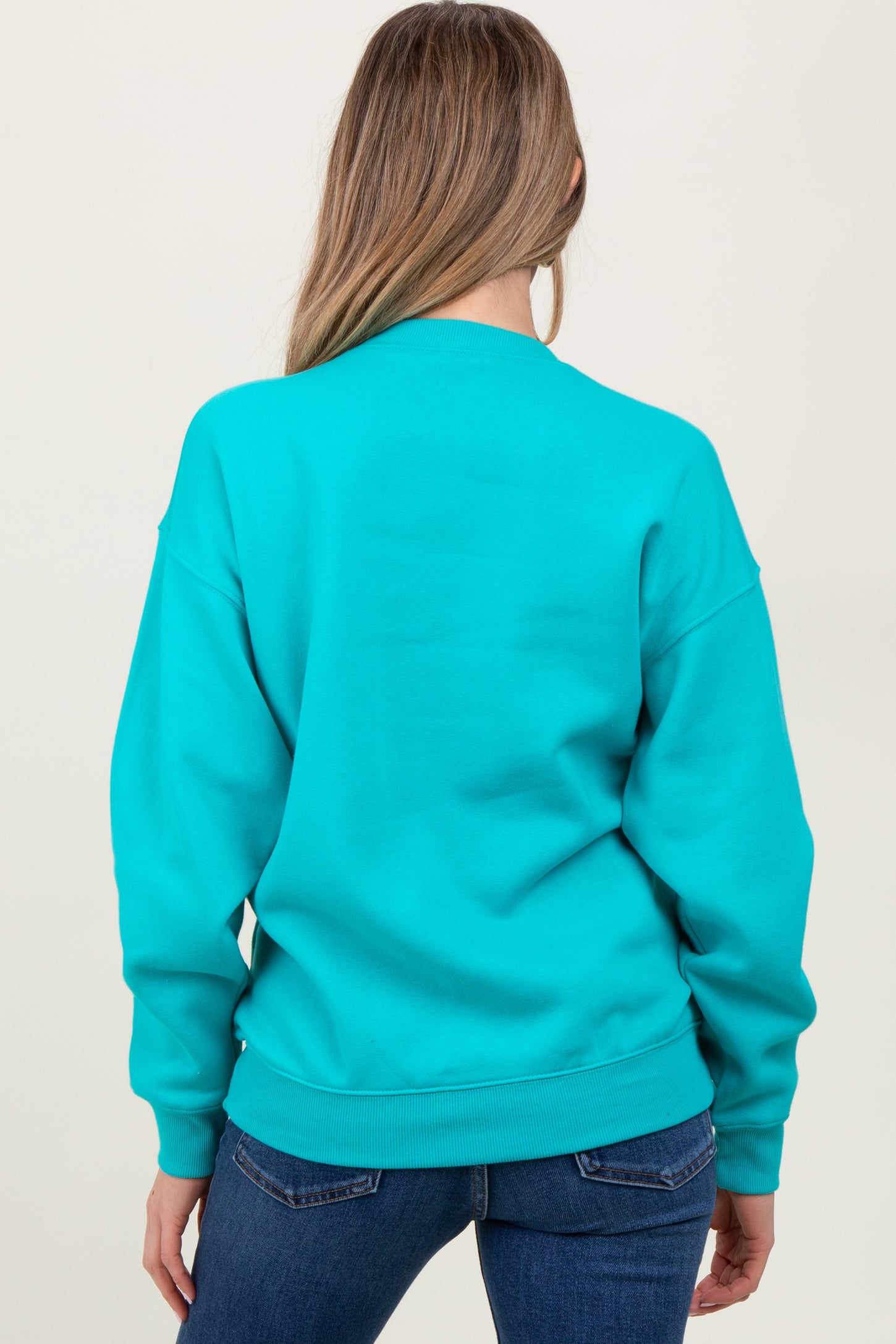 woman wearing a turquoise oversized maternity sweatshirt, shown from the back, paired with dark jeans