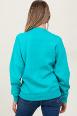 woman wearing a turquoise oversized maternity sweatshirt, shown from the back, paired with dark jeans