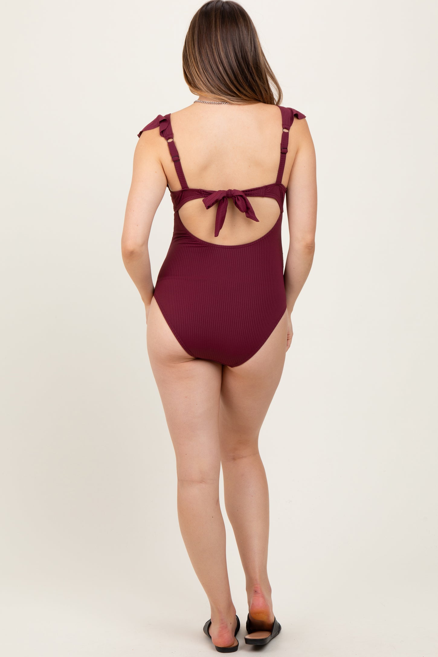 woman wearing a burgundy ribbed maternity swimsuit with tie straps and an open back