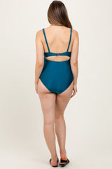 woman wearing a teal maternity swimsuit with adjustable straps and a cutout detail on the back
