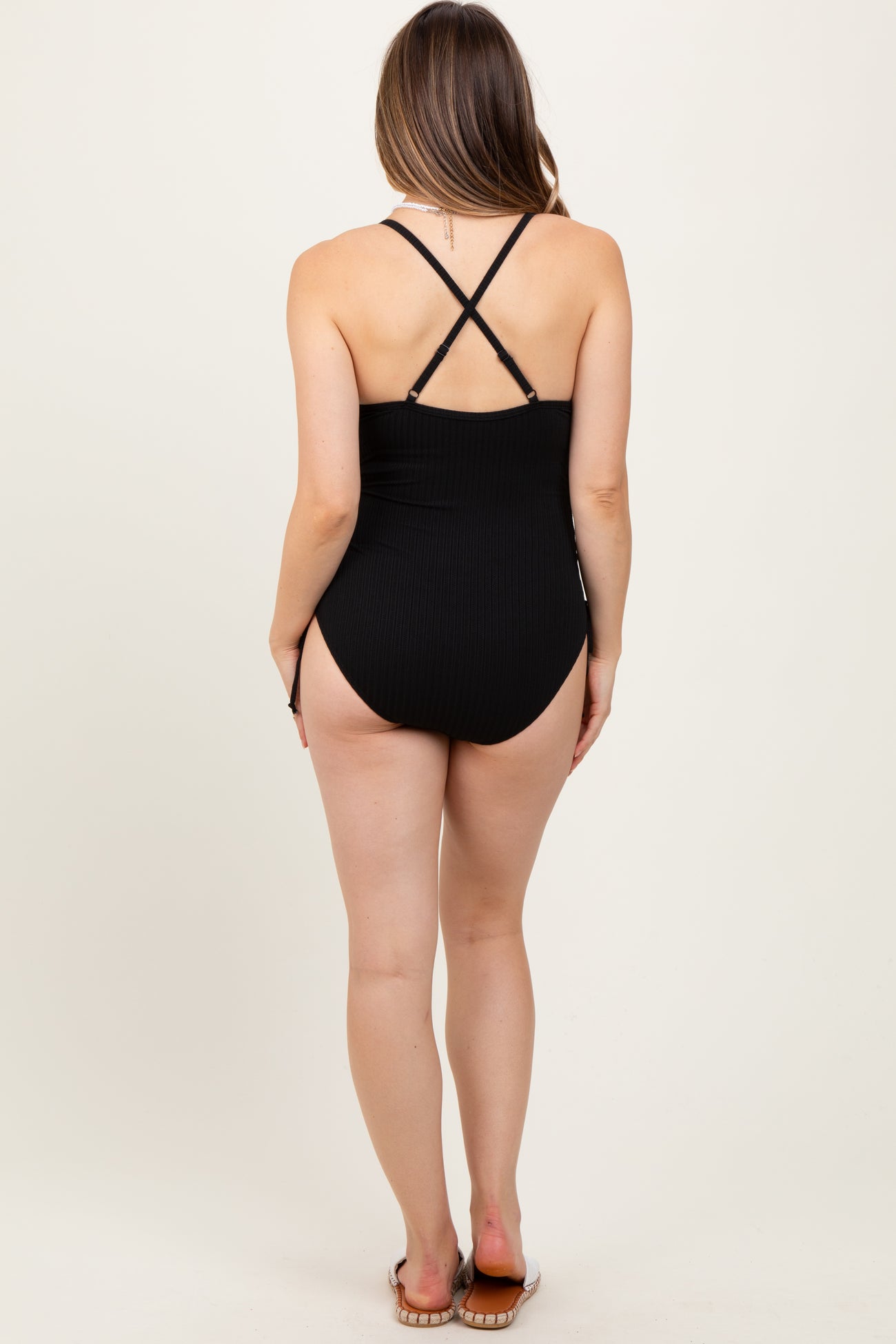 woman wearing a black ribbed maternity swimsuit with crossed straps, showing her back and legs