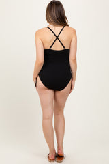 woman wearing a black ribbed maternity swimsuit with crossed straps, showing her back and legs