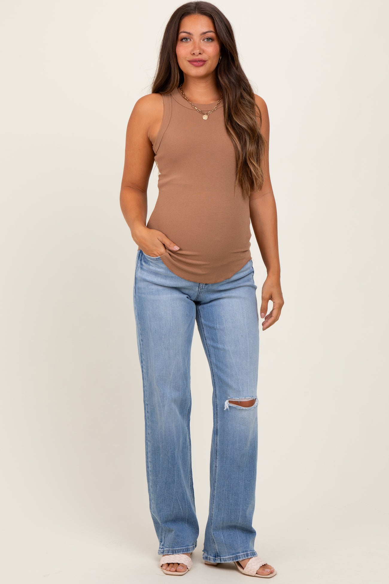 woman wearing a brown sleeveless maternity top and distressed light blue jeans with a visible baby bump