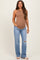 woman wearing a brown sleeveless maternity top and distressed light blue jeans with a visible baby bump