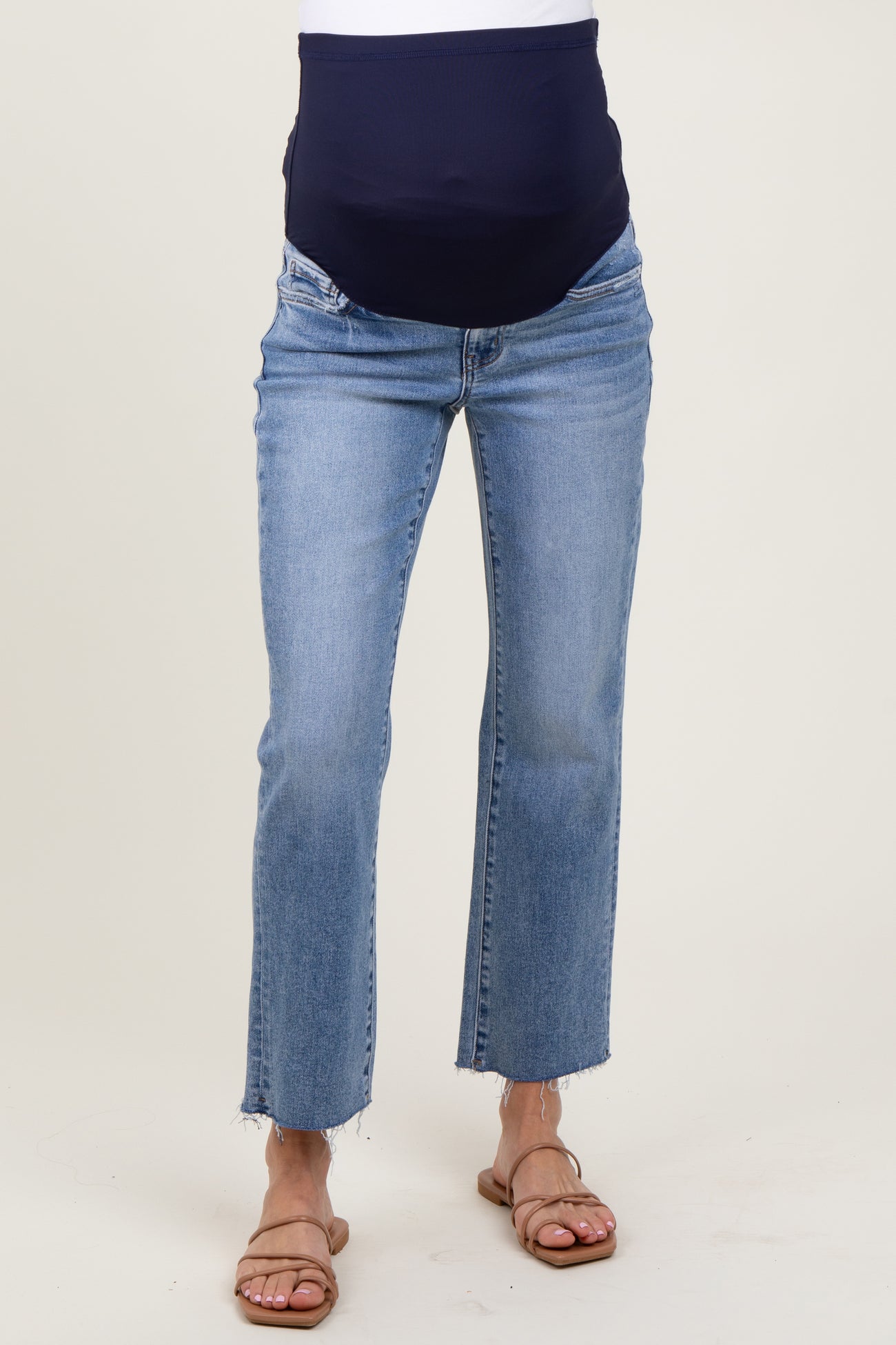 woman wearing blue maternity jeans with a navy over-the-bump panel and cropped raw hem, styled with sandals
