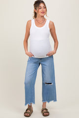 woman wearing a white ribbed maternity tank top and distressed light blue maternity jeans with a visible baby bump