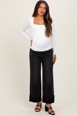 woman wearing a white long sleeve maternity top and black wide leg jeans with a visible baby bump