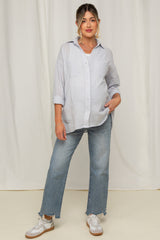woman wearing a light blue maternity button-up shirt and distressed jeans, with a visible baby bump