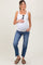 woman wearing a white tank top and blue maternity jeans, holding her baby bump, standing casually with sunglasses in hand