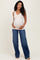 woman wearing a beige maternity tank top and blue wide-leg jeans, showing her baby bump while smiling