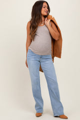 woman wearing a beige maternity tank top and light blue flared jeans, showcasing her baby bump, with a tan jacket draped over her shoulder