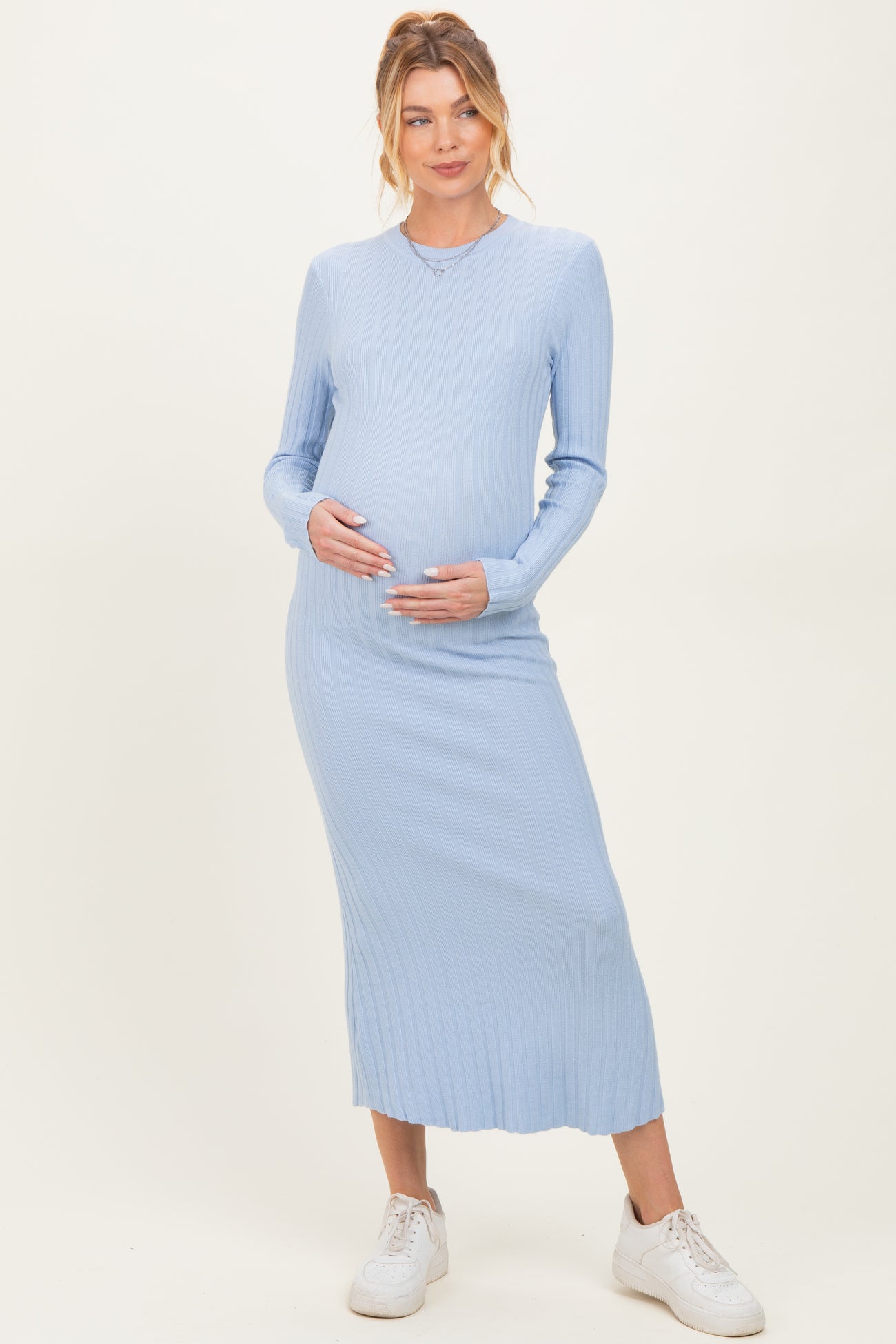 woman wearing a light blue ribbed maternity dress with long sleeves and a visible baby bump, holding her belly