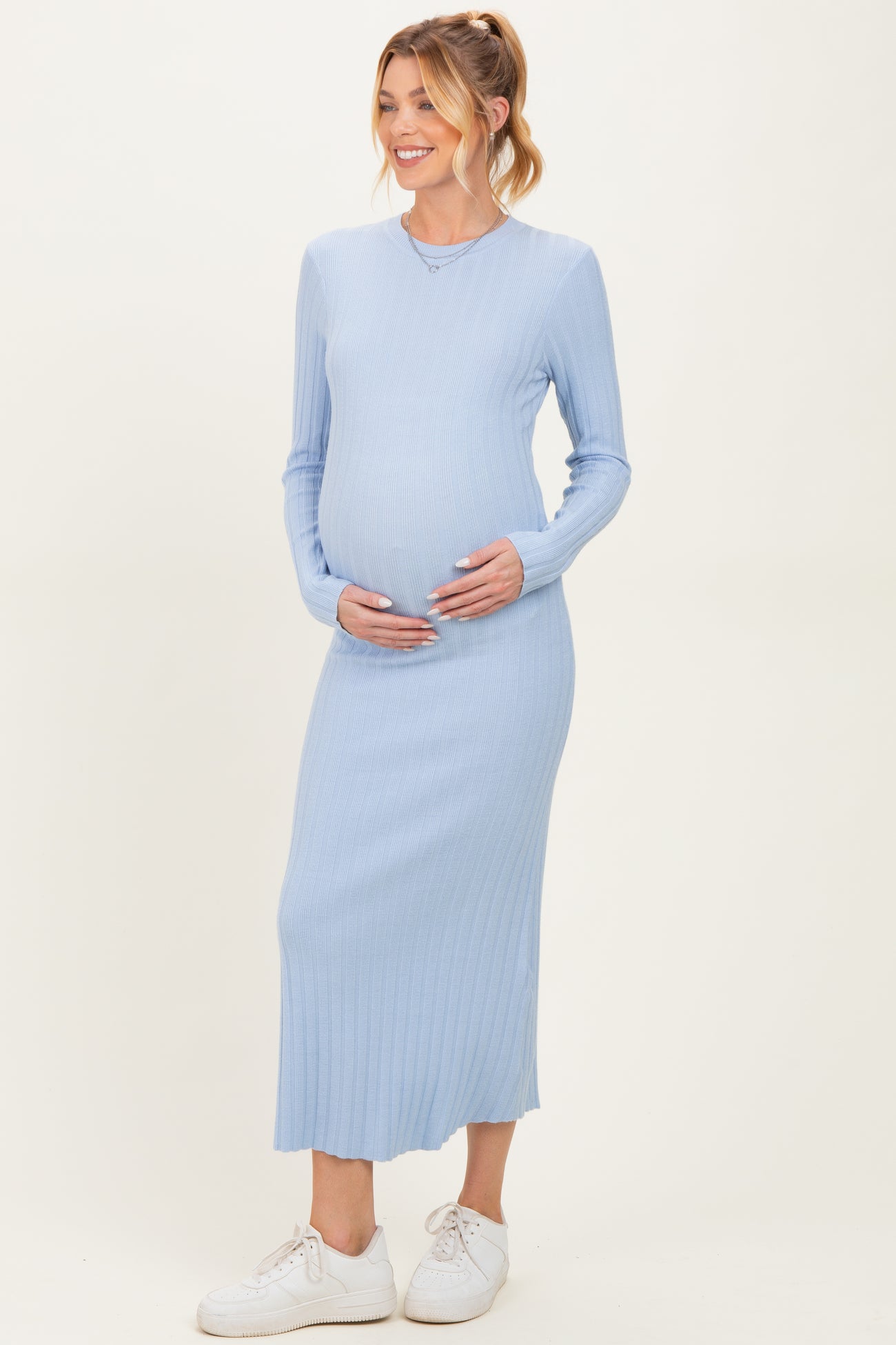 woman wearing a light blue ribbed long sleeve maternity dress and holding her baby bump