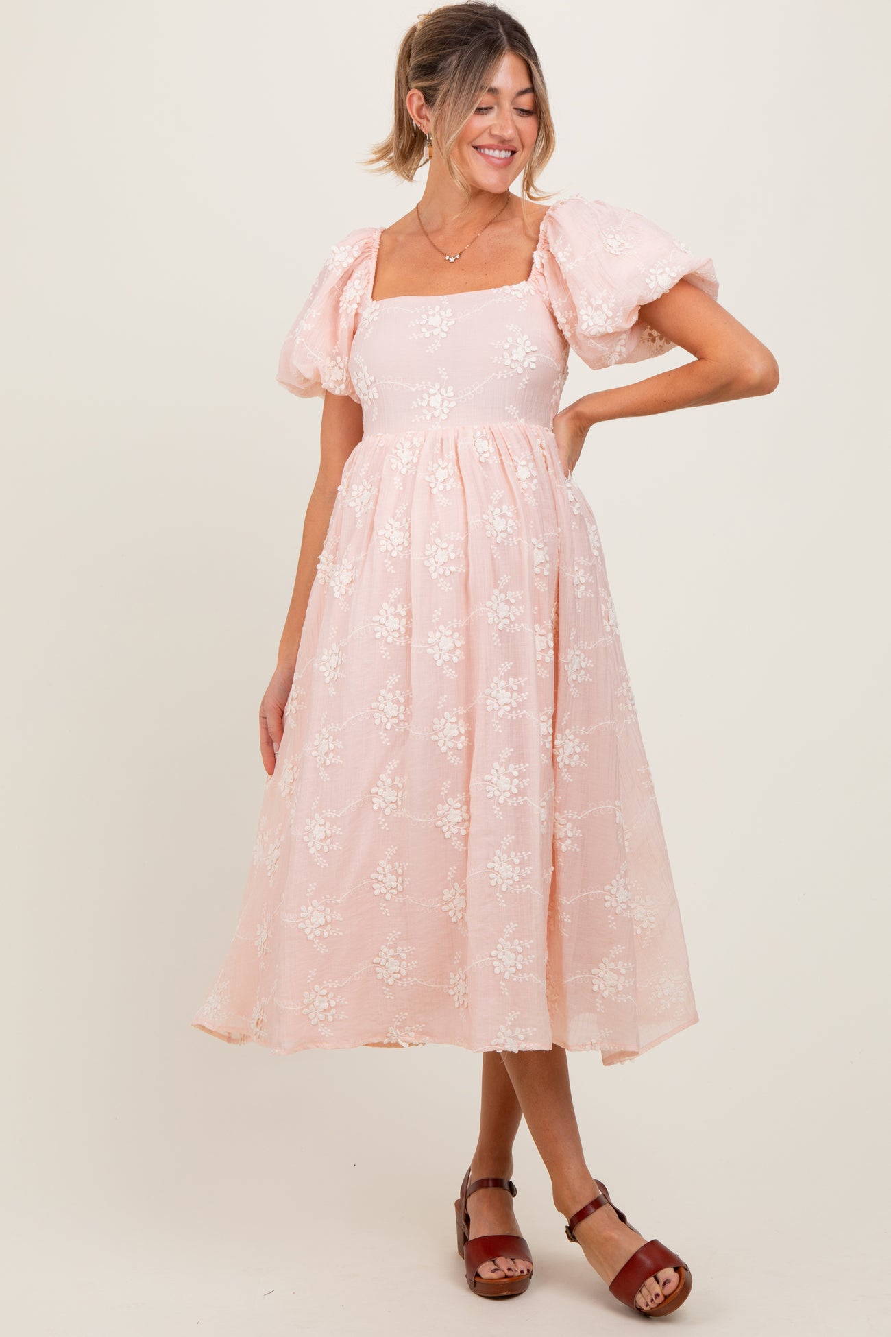 woman wearing a light pink floral maternity dress with puff sleeves and a flowing skirt, showcasing a baby bump