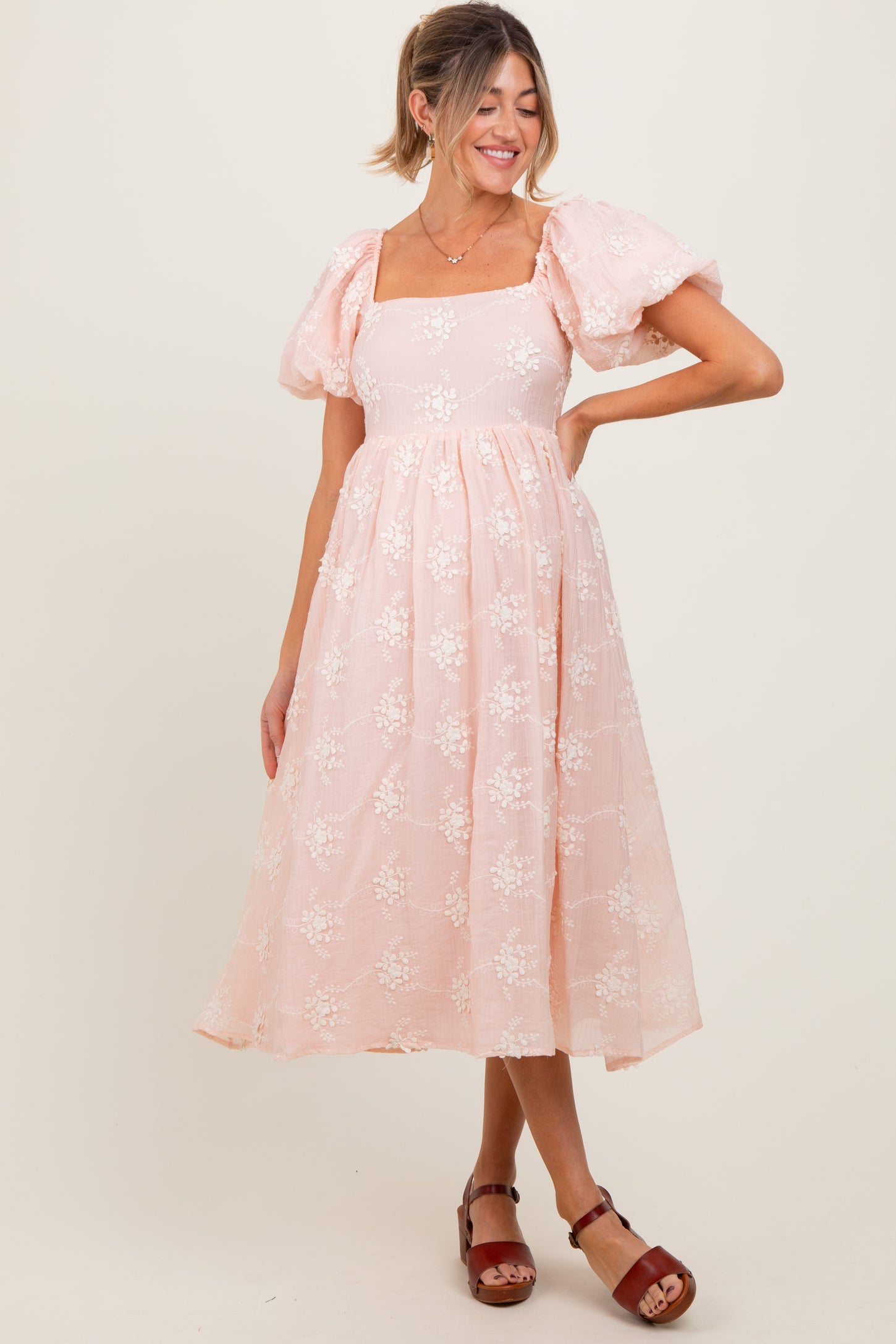 woman wearing a light pink floral maternity dress with puff sleeves and a flowing skirt, showcasing a baby bump